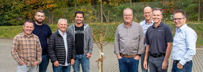Eight men standing in a field with a tree in the middle – all partners of AKL-tec.