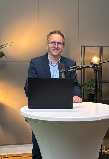 A CEO standing behind a bar table with a laptop and microphone for a video shoot
