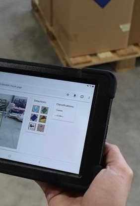 Mitarbeiter hält Tablet in der Hand und sieht Kisten und die Funktionsweise von Predictive Vision for Logistics