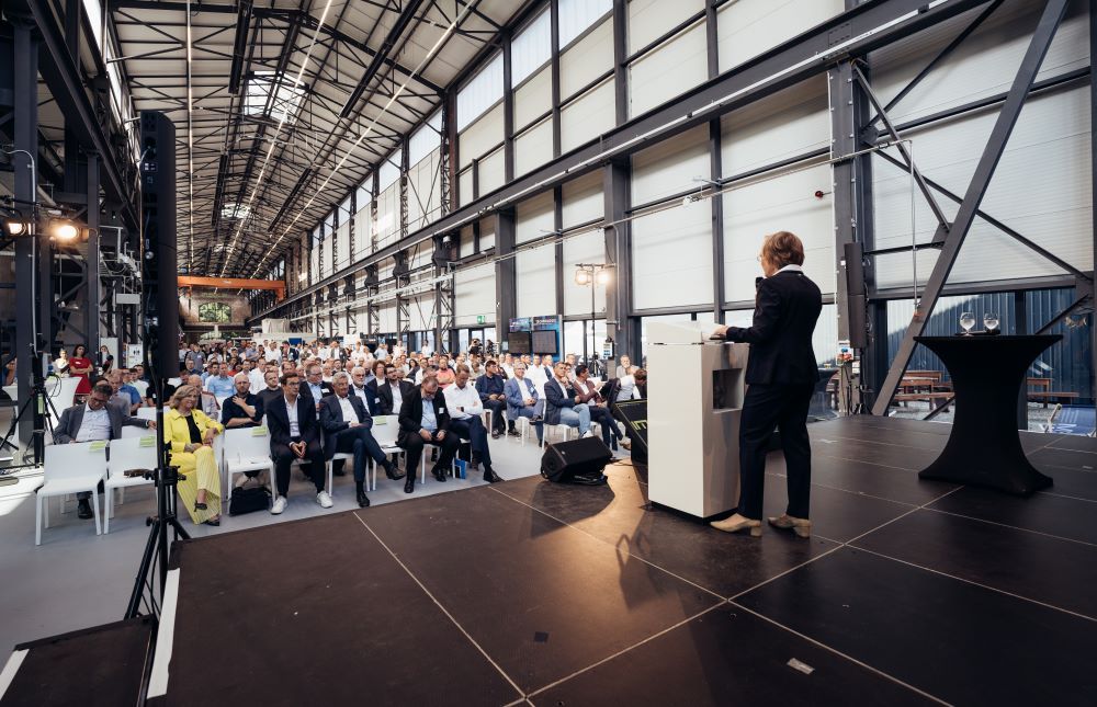 Frau steht auf einer Bühne der Smarten Demonstrationsfabrik in Siegen und spricht zum Publikum